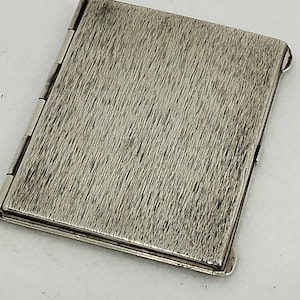 May include: A silver compact mirror with a textured surface and a hinged lid.