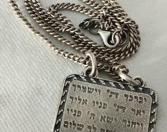 May include: Silver pendant necklace featuring a rectangular pendant with Hebrew script and a decorative border. The curb chain is approximately 50 cm in length.