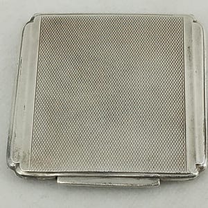 Puede incluir: Un estuche de cigarrillos de plata con una superficie texturizada y una tapa con bisagras.