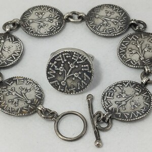 Puede incluir: Un conjunto de pulsera y anillo plateados. La pulsera presenta siete colgantes circulares con un diseño de árbol y detalles grabados. El anillo tiene un diseño similar. El conjunto es de metal y tiene un aspecto vintage.