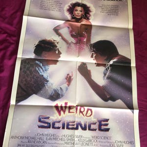 May include: A vintage movie poster for "Weird Science" featuring a woman in a pink dress and two men. The title is in a blue and silver font. The poster includes text about the movie's plot and credits.