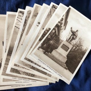 Könnte beinhalten: Eine Sammlung von Vintage-Postkarten in Schwarzweiß mit Londoner Wahrzeichen. Die Postkarten zeigen das Captain Scott Memorial, das Camel Corps Memorial und den Wellington Arch. Die Postkarten sind auf einer blauen Oberfläche fächerförmig angeordnet.