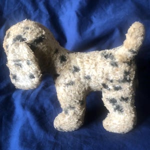 Può includere: Un giocattolo per cani di peluche vintage con un corpo color crema e macchie nere. Il cane ha orecchie flosce e una piccola coda. Il giocattolo è fatto di un materiale sfocato ed è in posa a quattro zampe.