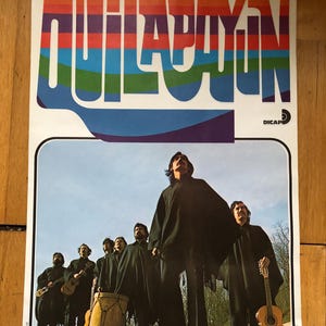 Könnte beinhalten: Vintage-Poster mit der Band Quilapayún. Die Bandmitglieder tragen schwarze Kleidung und stehen auf einer Steinstruktur. Der Titel des Posters ist in Regenbogenfarben gehalten. Gitarren und eine Trommel sind zu sehen.