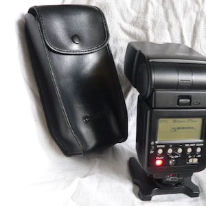 May include: A black Canon Speedlite 580EX flash unit with a built-in LCD screen and a black leather carrying case.