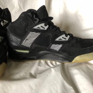 Puede incluir: Zapatillas deportivas altas negras con una textura similar al ante. Las zapatillas presentan detalles blancos, un diseño a rayas y una suela de color claro. El logotipo de Nike es visible.