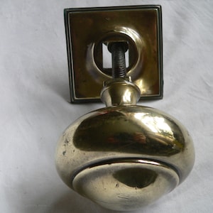 May include: A polished brass door knob with a square backplate. The knob is round and has a raised rim.