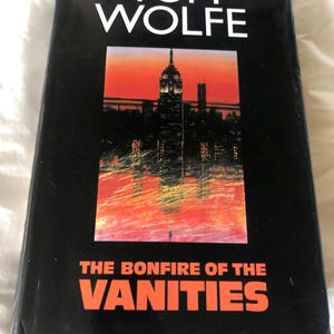 May include: A black hardcover book by Tom Wolfe, titled "The Bonfire of the Vanities" in orange lettering. The cover shows a cityscape with a red and orange sky.