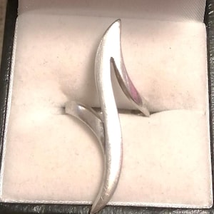 Peut inclure: Une bague argentée au design fluide et unique. La bague présente une forme incurvée et allongée qui s'enroule autour du doigt. La bague est présentée dans un écrin noir et blanc.