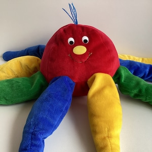May include: A plush red octopus toy with a smiling face, yellow nose, and blue eyes. The octopus has eight tentacles, each a different color: blue, green, yellow, and red.