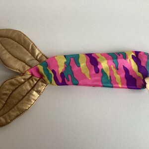Peut inclure: Une queue de sir&egrave;ne jouet avec une nageoire dor&eacute;e et un corps &agrave; motif camouflage rose, jaune, turquoise et violet. La queue est con&ccedil;ue pour le jeu des enfants et les d&eacute;guisements imaginatifs.