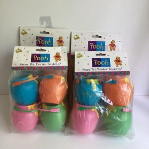 May include: Two clear plastic packages each containing four small plastic pots in blue, orange, pink, and green. The packaging features the text Pooh Hunny Pot Easter Baskets and an illustration of Winnie the Pooh. Each pot has a small handle.