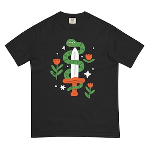 May include: Black t-shirt with a colourful graphic design. A green snake is wrapped around a white sword with an orange hilt. The design includes orange flowers, white stars, and green leaves. The shirt is made of a soft, comfortable material.