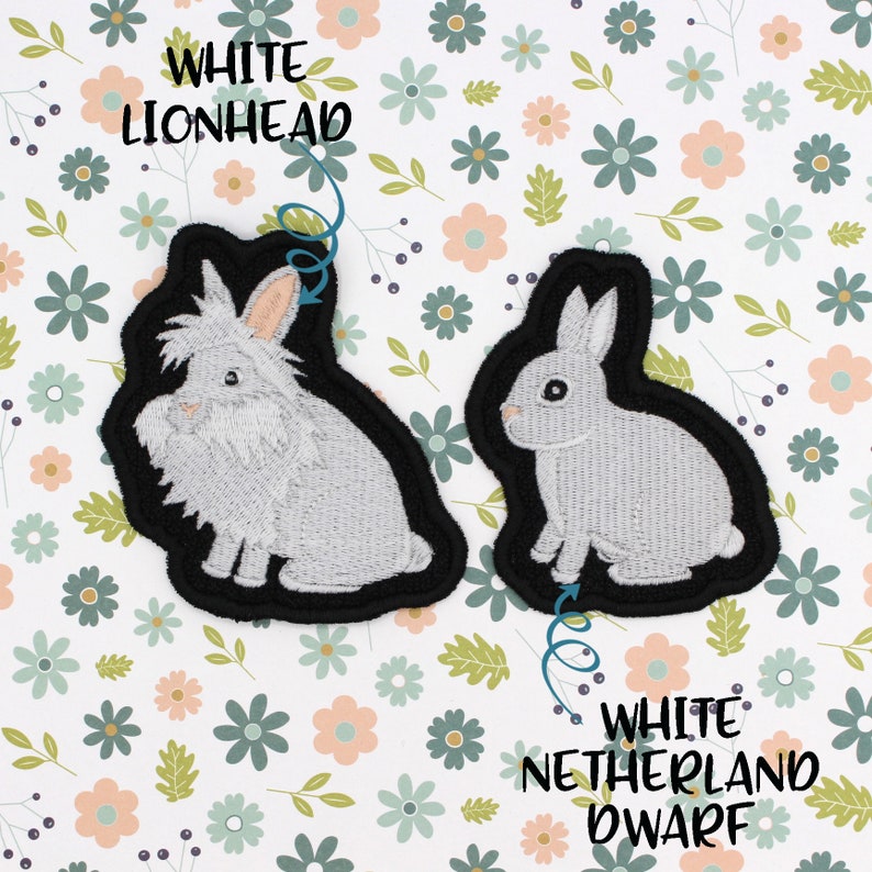 May include: Two white rabbit embroidered patches. The patch on the left is a white lionhead rabbit with the text "White Lionhead" above it. The patch on the right is a white Netherland Dwarf rabbit with the text "White Netherland Dwarf" below it.