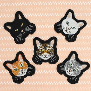 May include: Five embroidered iron-on patches featuring different cat breeds. The patches are black with white stitching and feature a black cat, a white cat, a tabby cat, an orange cat, and a gray cat.