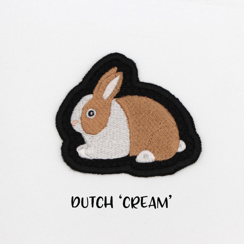 May include: Embroidered iron-on patch of a brown and white Dutch rabbit with black outline. The patch says "Dutch 'Cream'" below the rabbit.