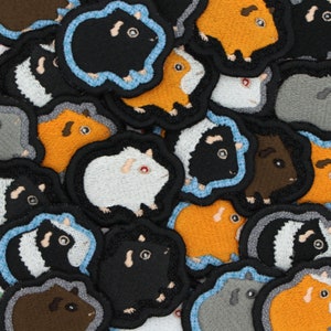 May include: A collection of colorful embroidered patches featuring various guinea pig designs. The patches are made of felt and have a variety of colors, including black, white, brown, orange, and gray. The patches are perfect for adding a touch of whimsy to clothing, bags, or other accessories.
