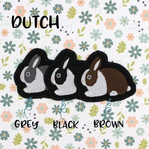 May include: Three embroidered iron-on patches of Dutch rabbits in grey, black, and brown. The patches are on a white background with a floral pattern.