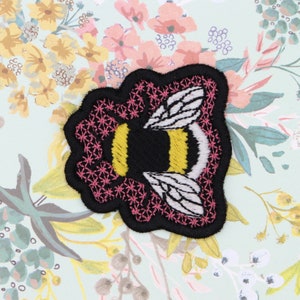 May include: Iron-on patch featuring an embroidered black and yellow bumblebee with white wings, surrounded by a pink flower design.