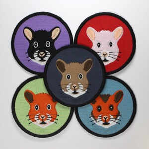 Pode incluir: Cinco patches redondos bordados com diferentes hamsters coloridos com olhos pretos. Os hamsters estão em um fundo branco. Os patches são roxo, vermelho, azul escuro, verde e azul.