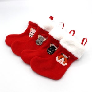 May include: Four red Christmas stockings with white fur trim and embroidered animal faces. The animals are a cat, a mouse, a fox, and a pink pig.
