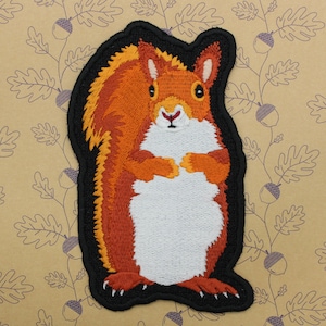 May include: Embroidered patch of a red squirrel with a white belly, standing on its hind legs with its paws together. The squirrel is surrounded by a black outline.