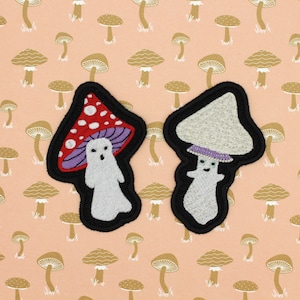 May include: Two embroidered iron-on patches of mushrooms with ghost faces. The mushroom on the left is red with white spots and a purple stem. The mushroom on the right is white with a purple stem.