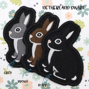 May include: Three embroidered iron-on patches of a rabbit in grey, brown, and black. The patches are labeled "Grey", "Brown", and "Black" and have the text "NETHERLAND DWARF" above them.