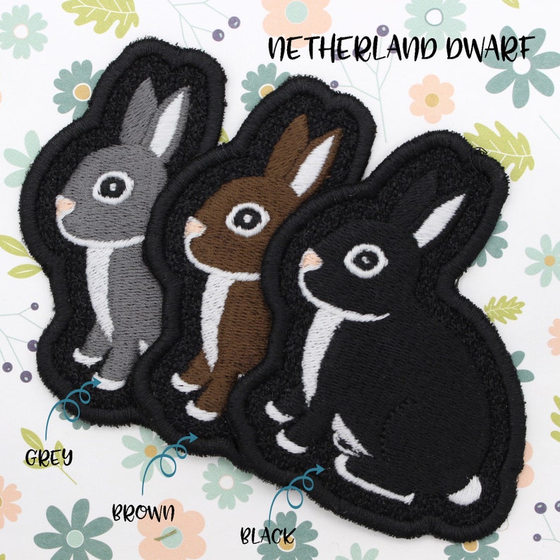 May include: Three embroidered iron-on patches of a rabbit in grey, brown, and black. The patches are labeled "Grey", "Brown", and "Black" and have the text "NETHERLAND DWARF" above them.