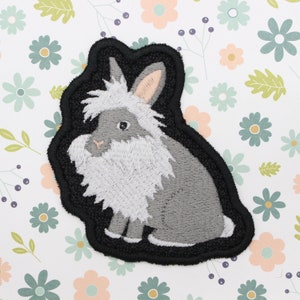 May include: A gray and white embroidered patch of a fluffy rabbit with a black outline.