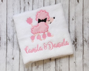 May include: White towel with pink and black embroidered poodle and the text "Camila & Daniela".