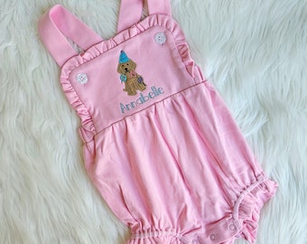 Könnte beinhalten: Rosaer Baby-Strampler mit Rüschenbesatz und gesticktem Hund, der einen Partyhut trägt. Der Strampler ist mit dem Namen "Annabelle" personalisiert.