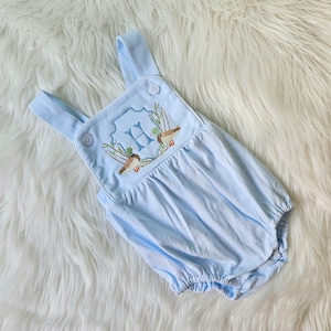 May include: A light blue baby onesie with a white button closure and embroidered ducks and the letter "H" on the front.