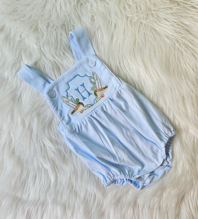 May include: A light blue baby onesie with a white button closure and embroidered ducks and the letter "H" on the front.