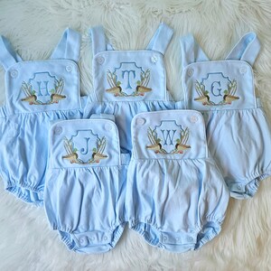 May include: Five light blue baby onesies with white trim and embroidered duck and letter designs. The letters are H, T, G, J, and W.