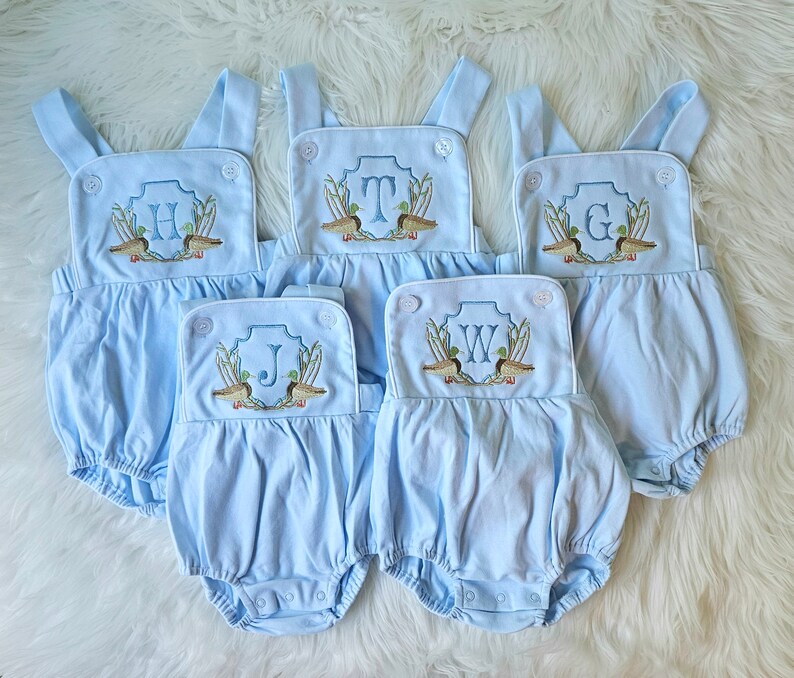 May include: Five light blue baby onesies with white trim and embroidered duck and letter designs. The letters are H, T, G, J, and W.