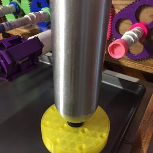 May include: A silver metal tube with a yellow plastic base with multiple holes. The tube is sitting on a gray metal surface.