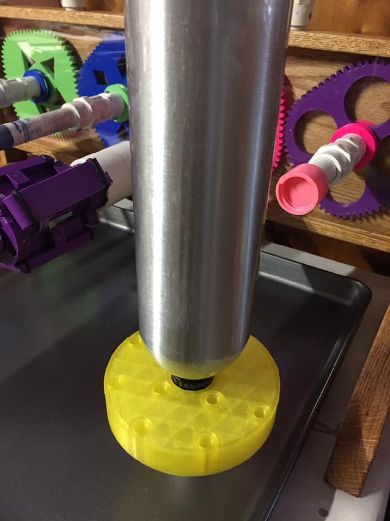 May include: A silver metal tube with a yellow plastic base with multiple holes. The tube is sitting on a gray metal surface.