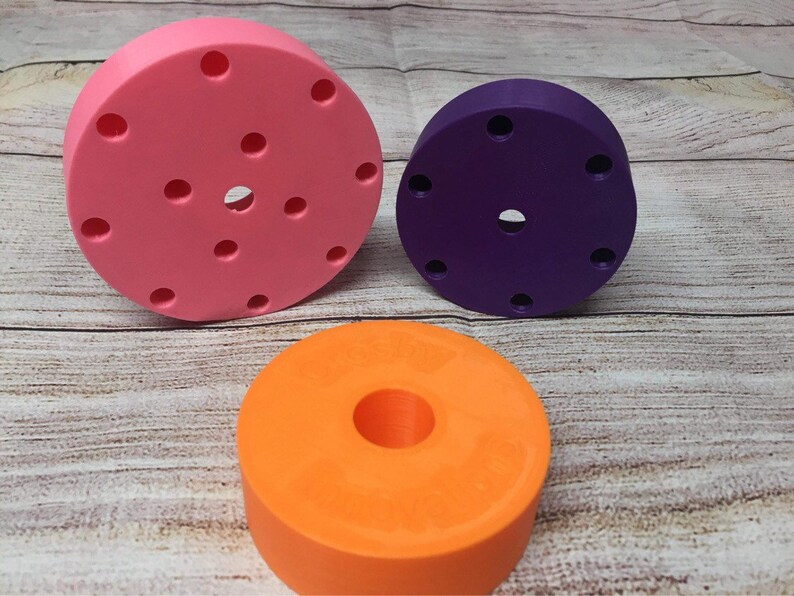 May include: Three round, colorful, plastic discs with different designs. The largest disc is pink with multiple holes, the middle disc is purple with a few holes, and the smallest disc is orange with a large hole in the center.