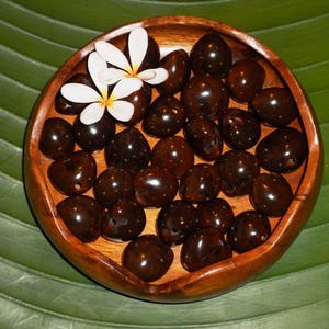 May include: A wooden bowl filled with dark brown Hawaiian coffee beans, decorated with white plumeria flowers.