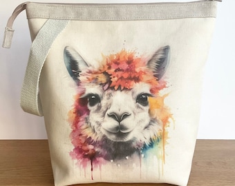 May include: A white canvas tote bag with a colorful watercolor illustration of an alpaca's face. The alpaca has a pink, orange, and yellow watercolor design around its head.