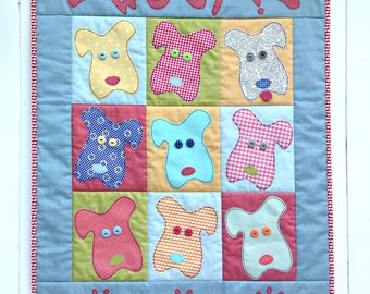 May include: A blue and white patchwork quilt with the word "WOOF!" in red letters. The quilt features nine squares with different colored and patterned dog faces. Each dog face has two button eyes and a red nose.