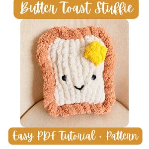May include: A plush toast-shaped pillow with a textured cream-colored center, a brown crust border, and a bright yellow butter square. It features a simple embroidered face with black eyes and a smile. Text reads: Butter Toast Stuffie Easy PDF Tutorial + Pattern.