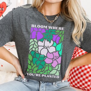 May include: A dark gray t-shirt with a colorful floral design and the text "Bloom Where You're Planted".