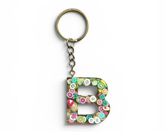 May include: A letter B keyring made of clear resin embedded with colourful miniature fruit slices including strawberries, kiwis, and citrus segments. The letter is attached to a circular metal split ring by a short silver-toned metal chain.