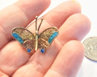 May include: A small silver butterfly brooch with blue enamel accents. The butterfly is about the size of a UK 20 pence coin.