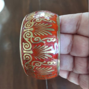 May include: A red and gold bangle bracelet with a decorative design. The bracelet is made of metal and has a shiny finish.