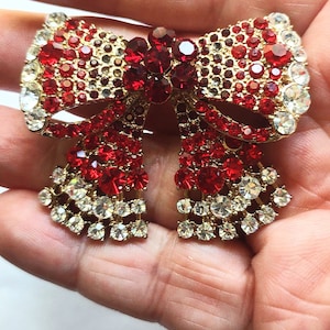 May include: A gold-tone brooch in the shape of a bow with red and clear rhinestones.
