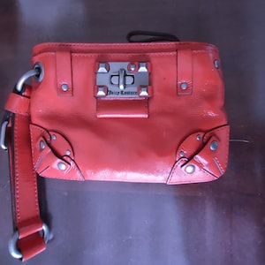 May include: A bright orange leather handbag with a silver lock and the words "Juicy Couture" on the front.