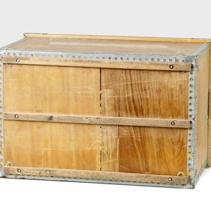 May include: A wooden storage box with metal trim and two wooden slats across the front. The box is made of light wood and has a worn, vintage look.